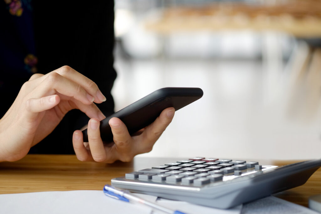 Closeup shot of a woman using a cellphone and working on her budget using a calculator