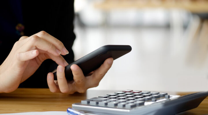 Closeup shot of a woman using a cellphone and working on her budget using a calculator